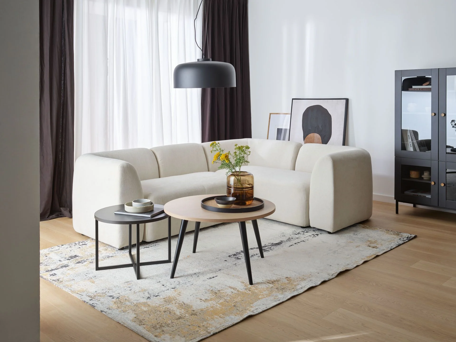 Nowoczesny, biały narożnik w minimalistycznym salonie z czarną lampą wiszącą i stolikami kawowymi